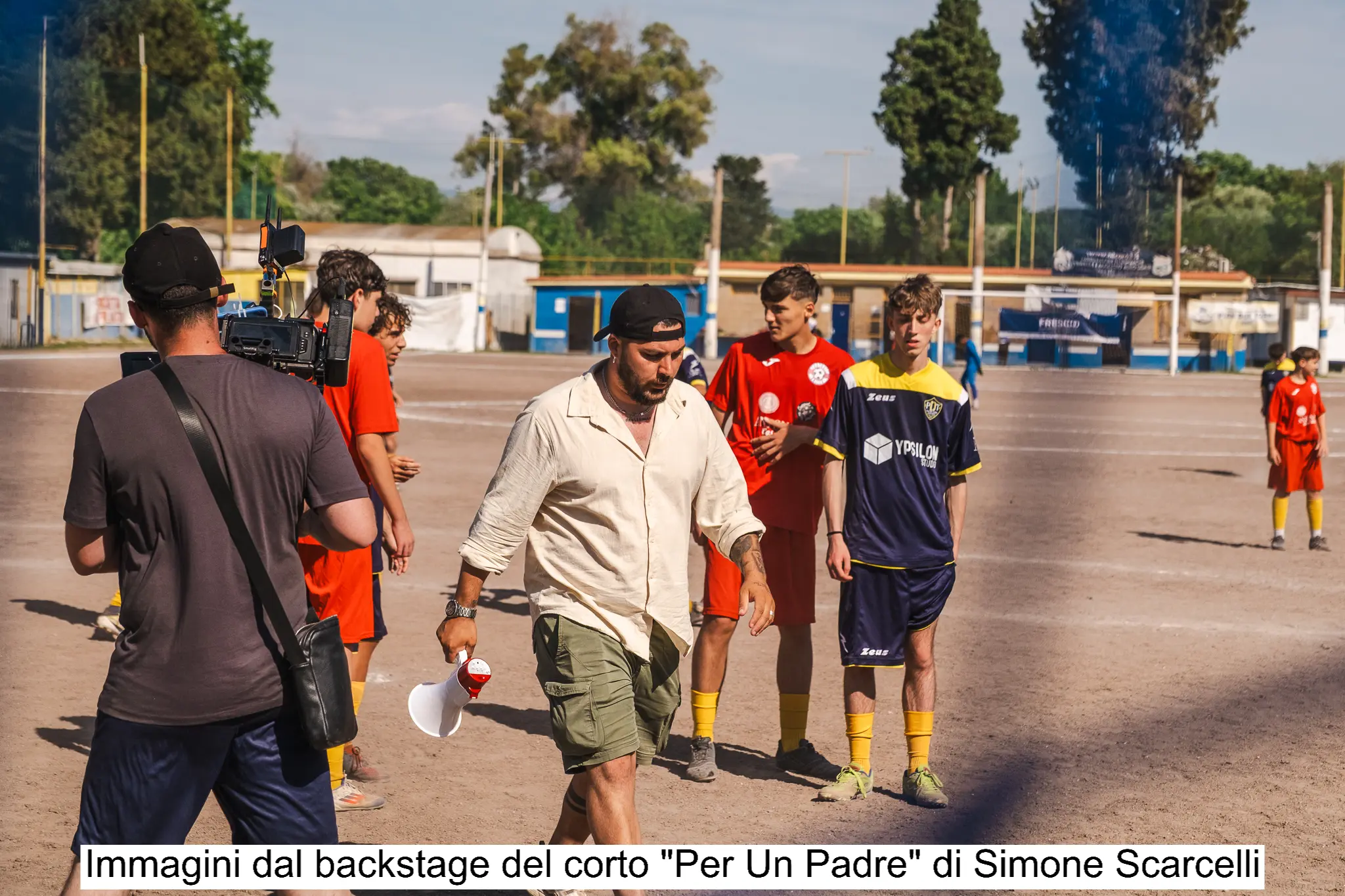 “Foto backstage di un cortometraggio girato in un centro sportivo, con troupe e attori durante le riprese su un campo da calcio.”