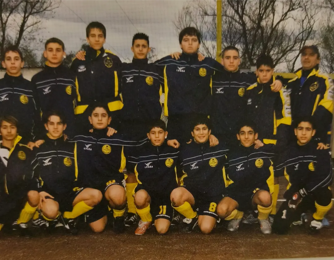 Gruppo di giovani calciatori del Pian Due Torri con tute nere e gialle, in posa insieme agli adulti dello staff sul campo da calcio.