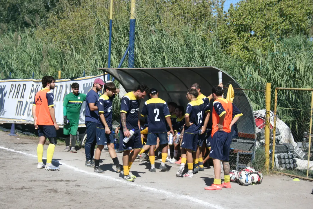 Calciatori e componenti dello staff del Pian Due Torri riuniti vicino alla panchina durante un momento di confronto sul campo.